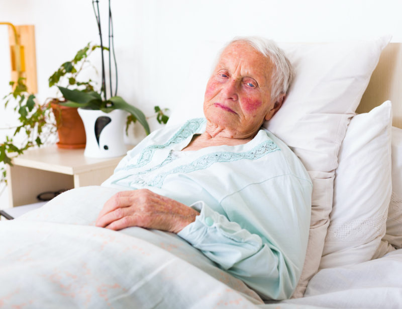 Tired elderly woman laying in bed alone in a nursing home.