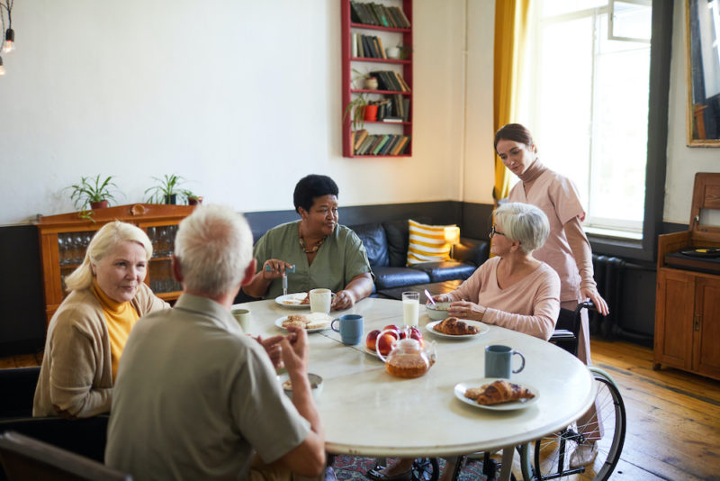 Warm-toned portrait of diverse group of senior people enjoying breakfast in cozy nursing home, copy space