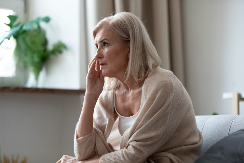 Pensive worried disappointed middle-aged woman seated on couch lost in sad thoughts looks to nowhere feels abandoned and lonely. Thinking about life personal or health problems, mental disease concept