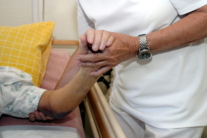 A nurse caring for and elderly woman in a nursing home with a bruise or bed sore on the elbow.